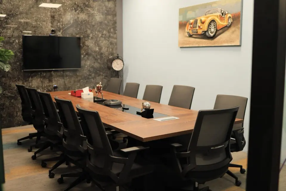 An empty meeting room with a long table, a wall screen and a clock.